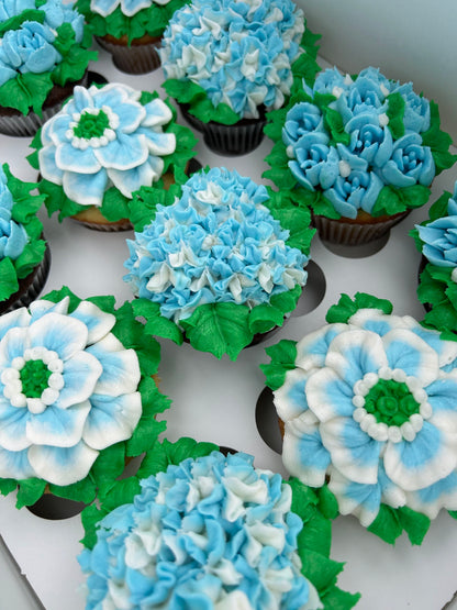 Cupcakes decorated with blue, white, and green icing to resemble flowers on a white background.
