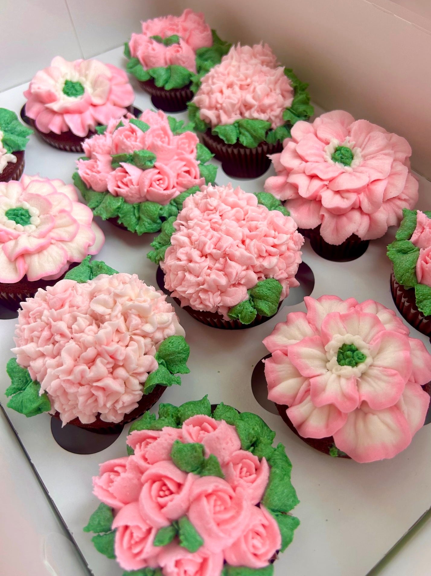 Cupcakes decorated with pink, white, and green icing to resemble flowers on a white background.