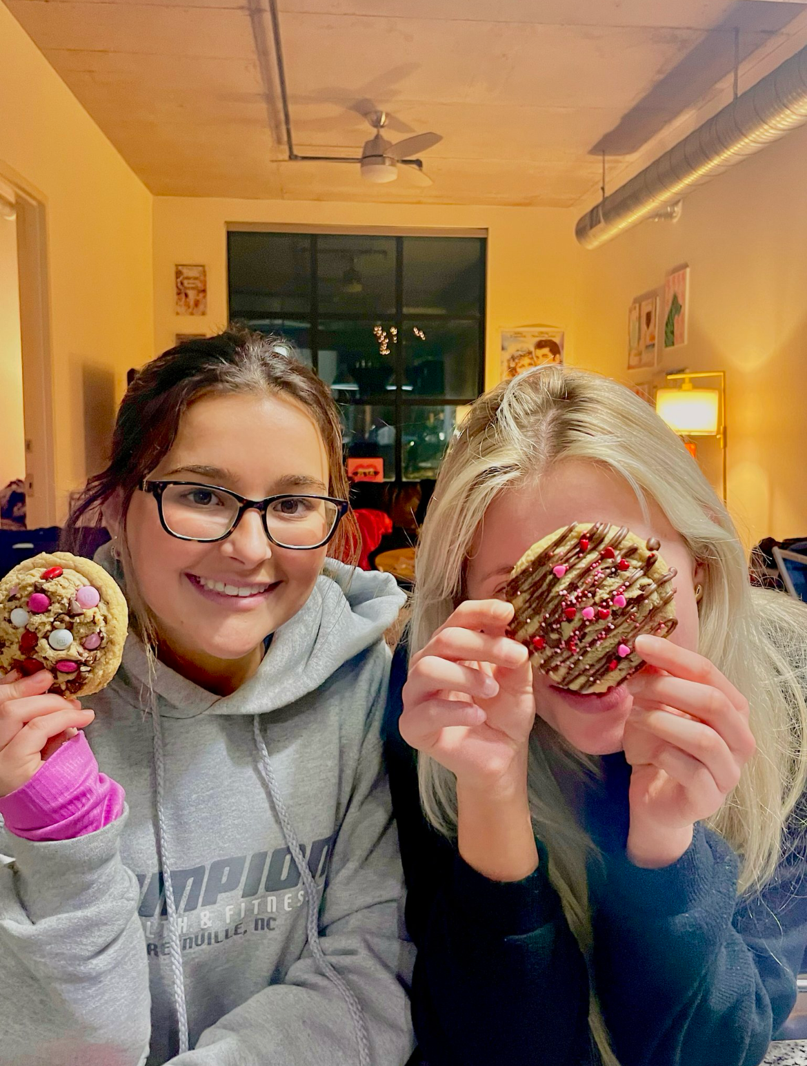 Two women holding Valentine's decorated cookies.