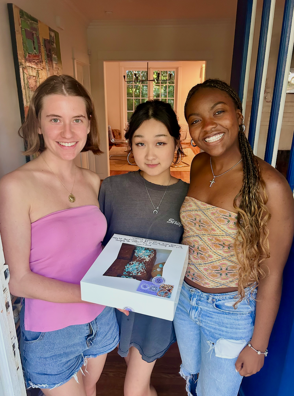 Three women holding a box of brownies and cookies.