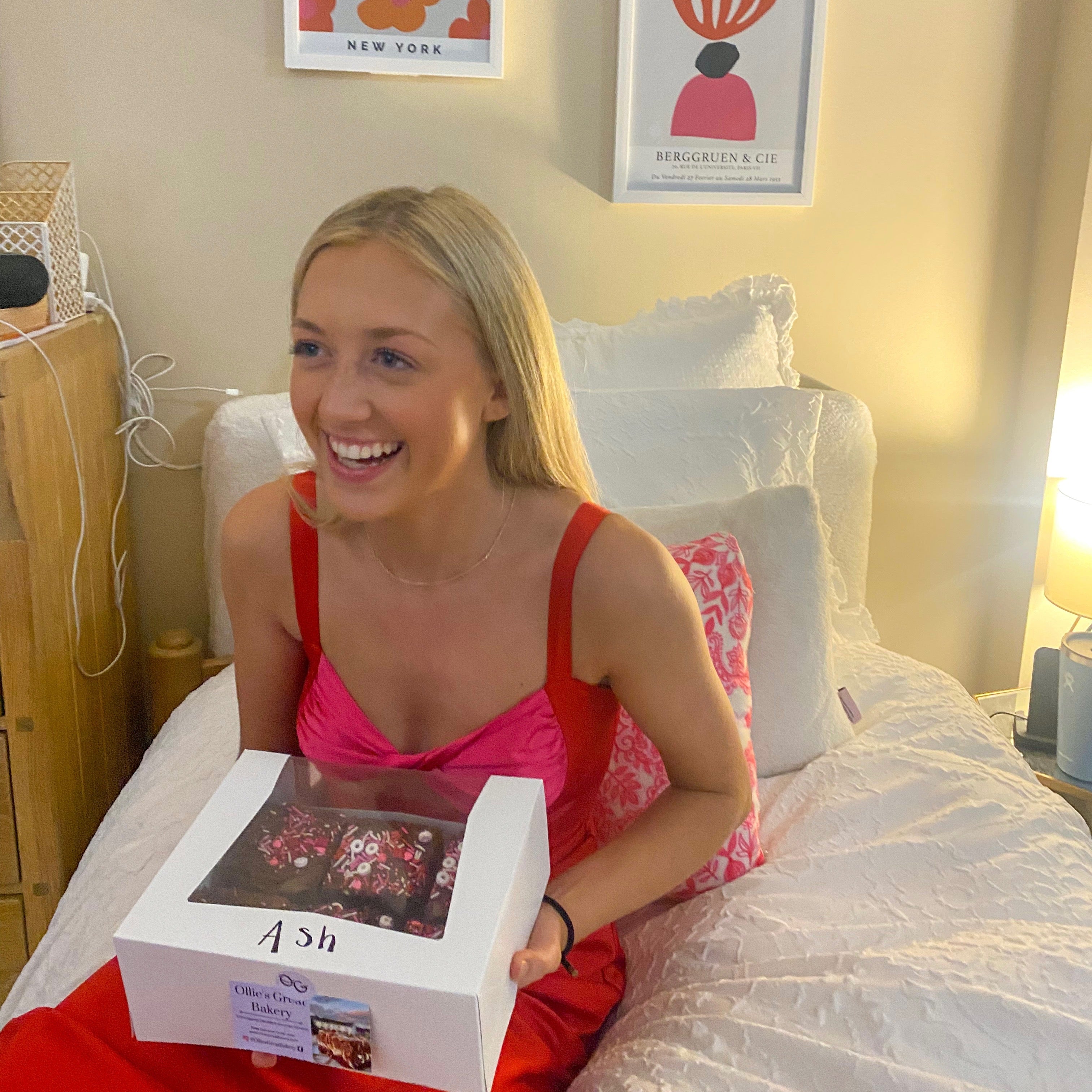 Woman in a red dress holding a box of brownies in her dorm room.