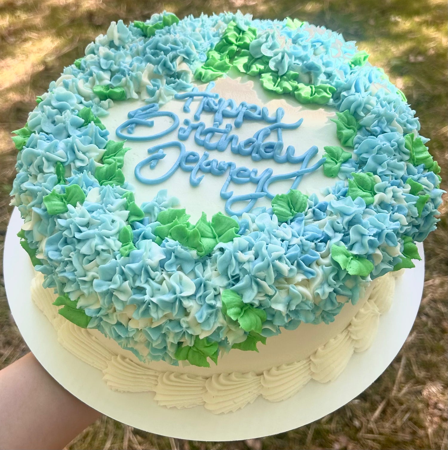 Birthday cake with blue and green hydrangea border and 'Happy Birthday Delaney' text.
