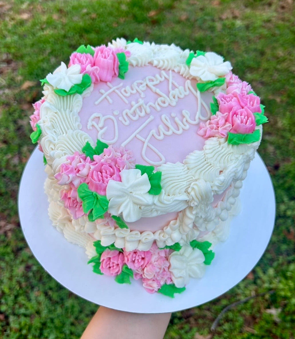 Decorative birthday cake with pink and white flowers and 'Happy Birthday Julie' text.