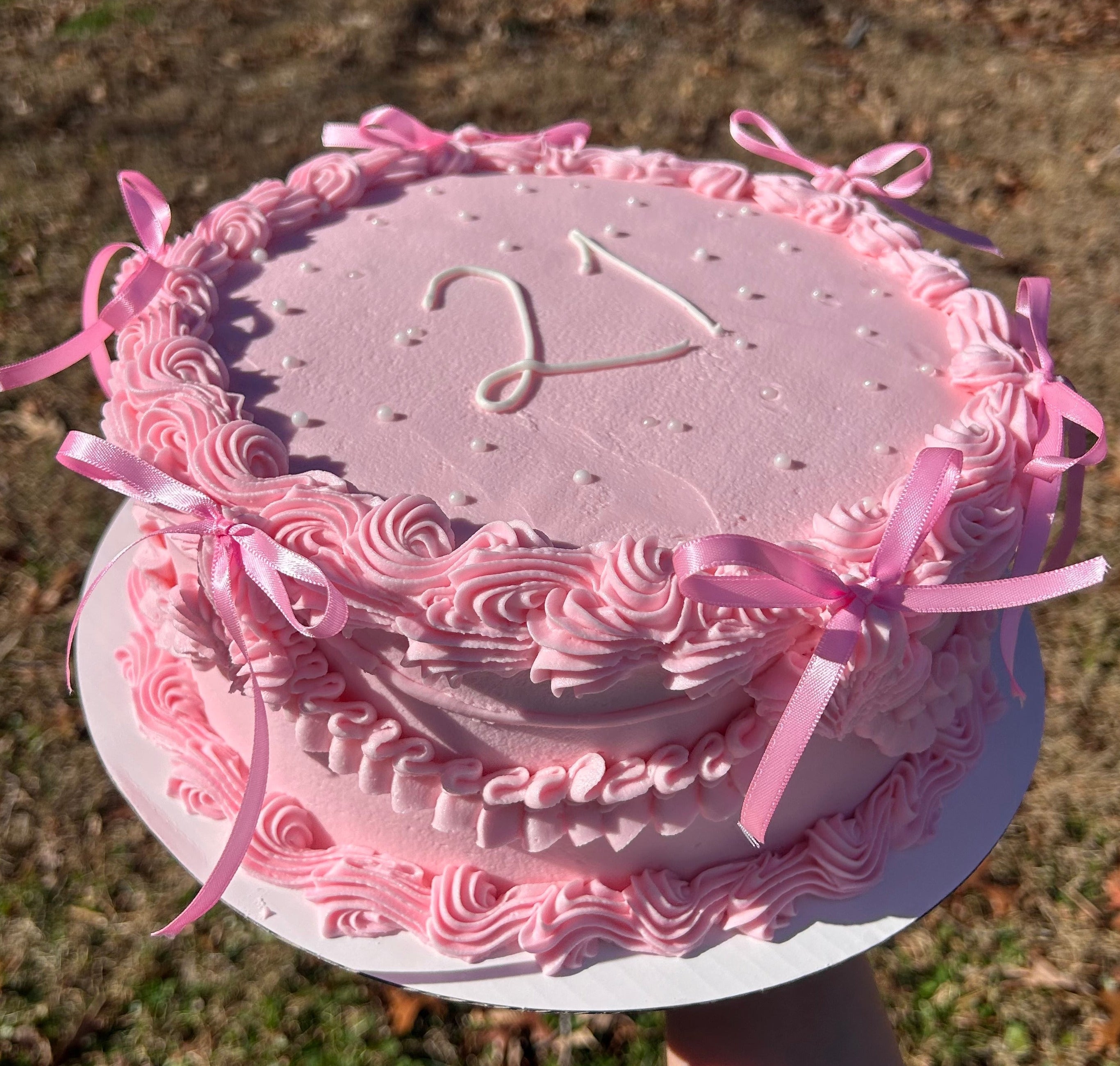 Pink birthday cake with number pink bows, white pearls, and '21' text.