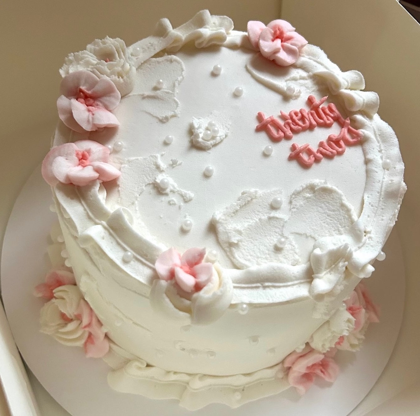 White cake with pink flowers and 'twenty two' text in pink.