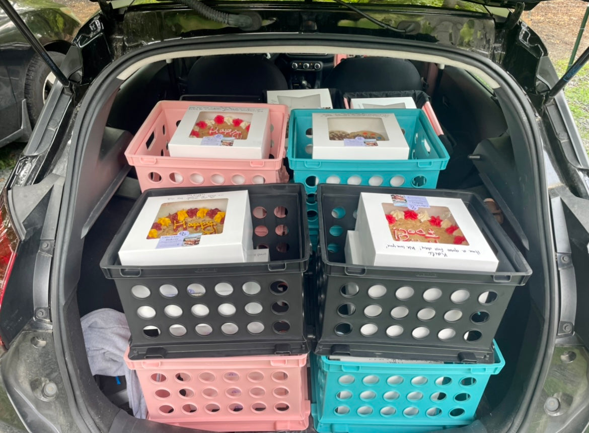 Several storage crates stacked inside the open trunk of a car, each holding white bakery boxes.