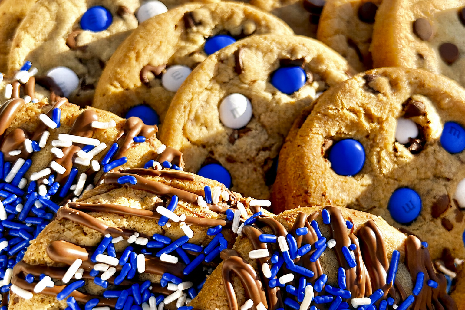 Close-up of royal blue M&M cookies and royal blue sprinkle cookies with chocolate drizzle.