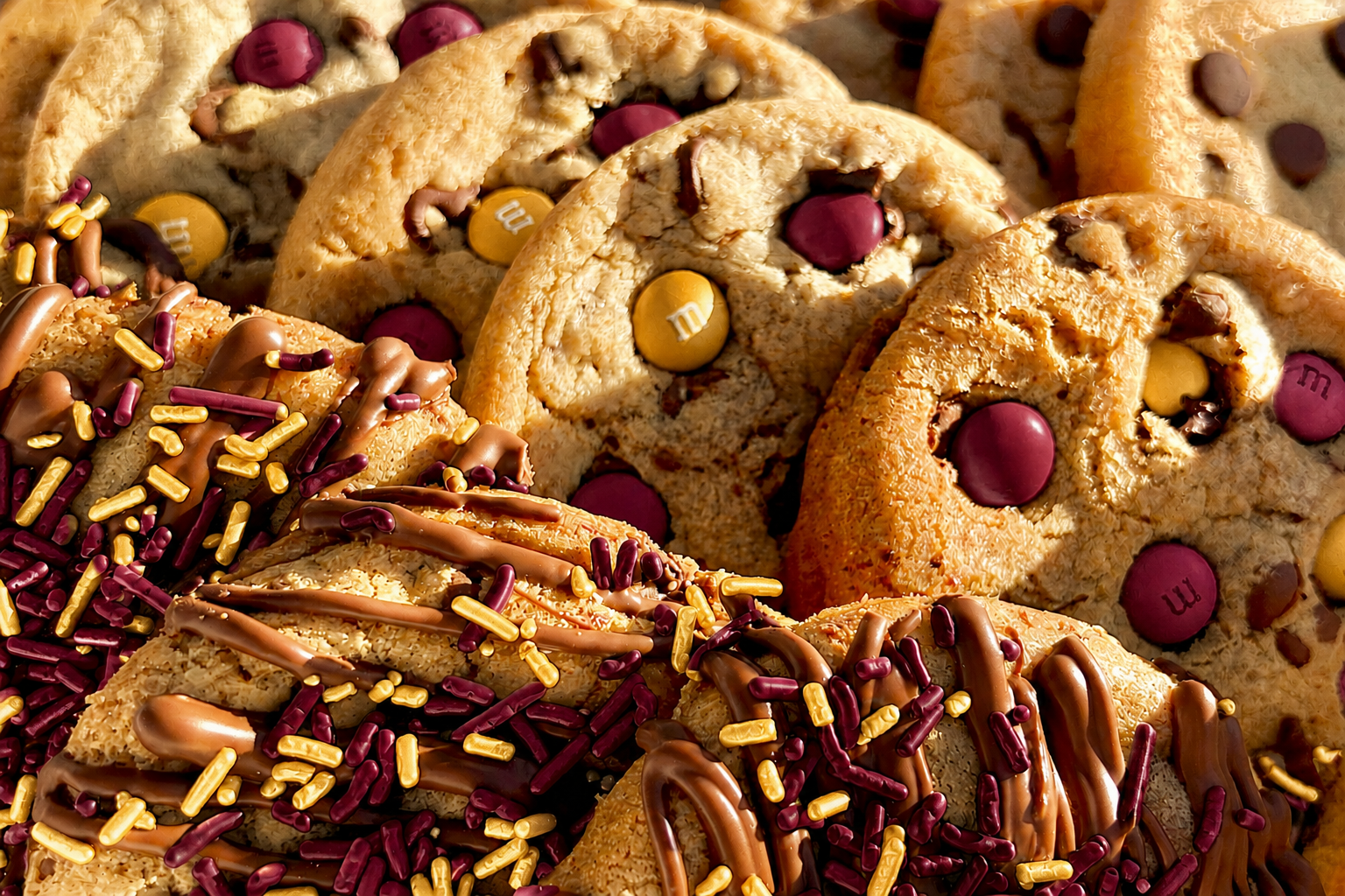 Close-up of maroon and gold M&M cookies and maroon and gold sprinkle cookies with chocolate drizzle.