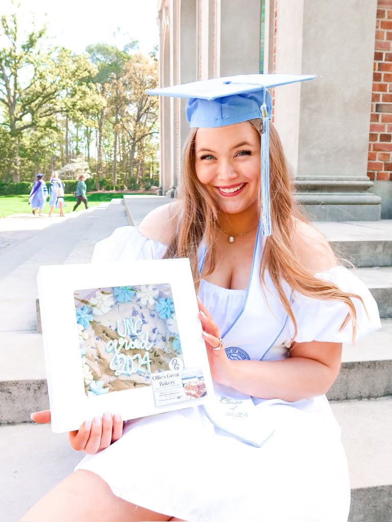 Graduation photo of a UNC graduate holding a light blue and white 'UNC Grad 2024' cookie cake