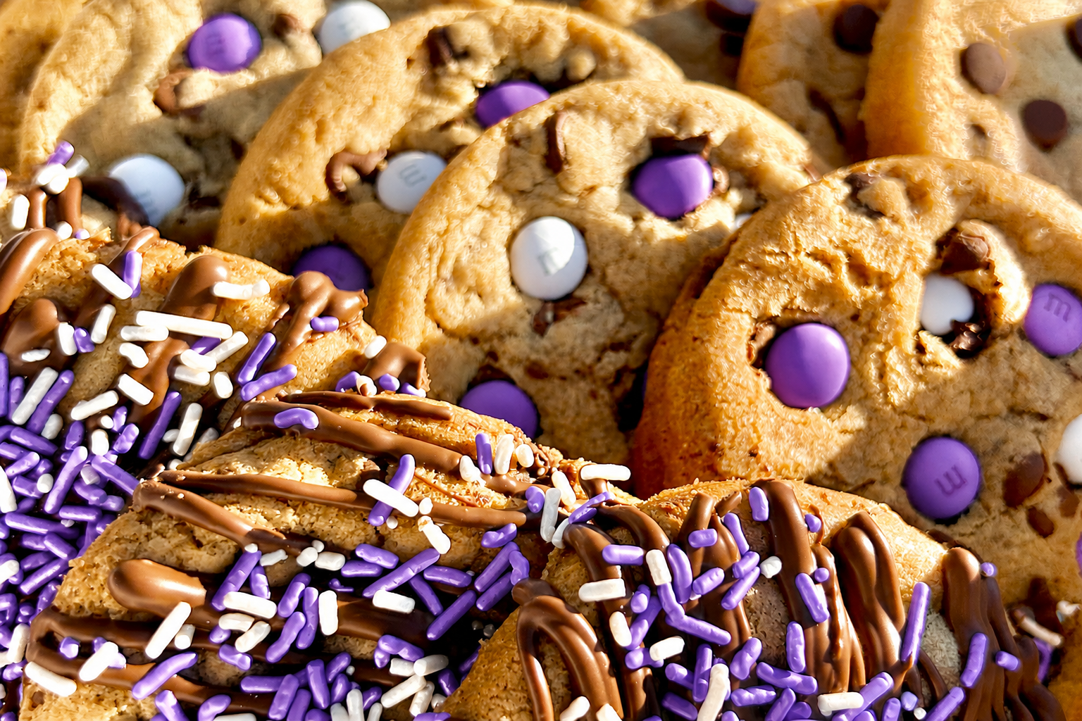 Close-up of purple M&M cookies and purple sprinkle cookies with chocolate drizzle.