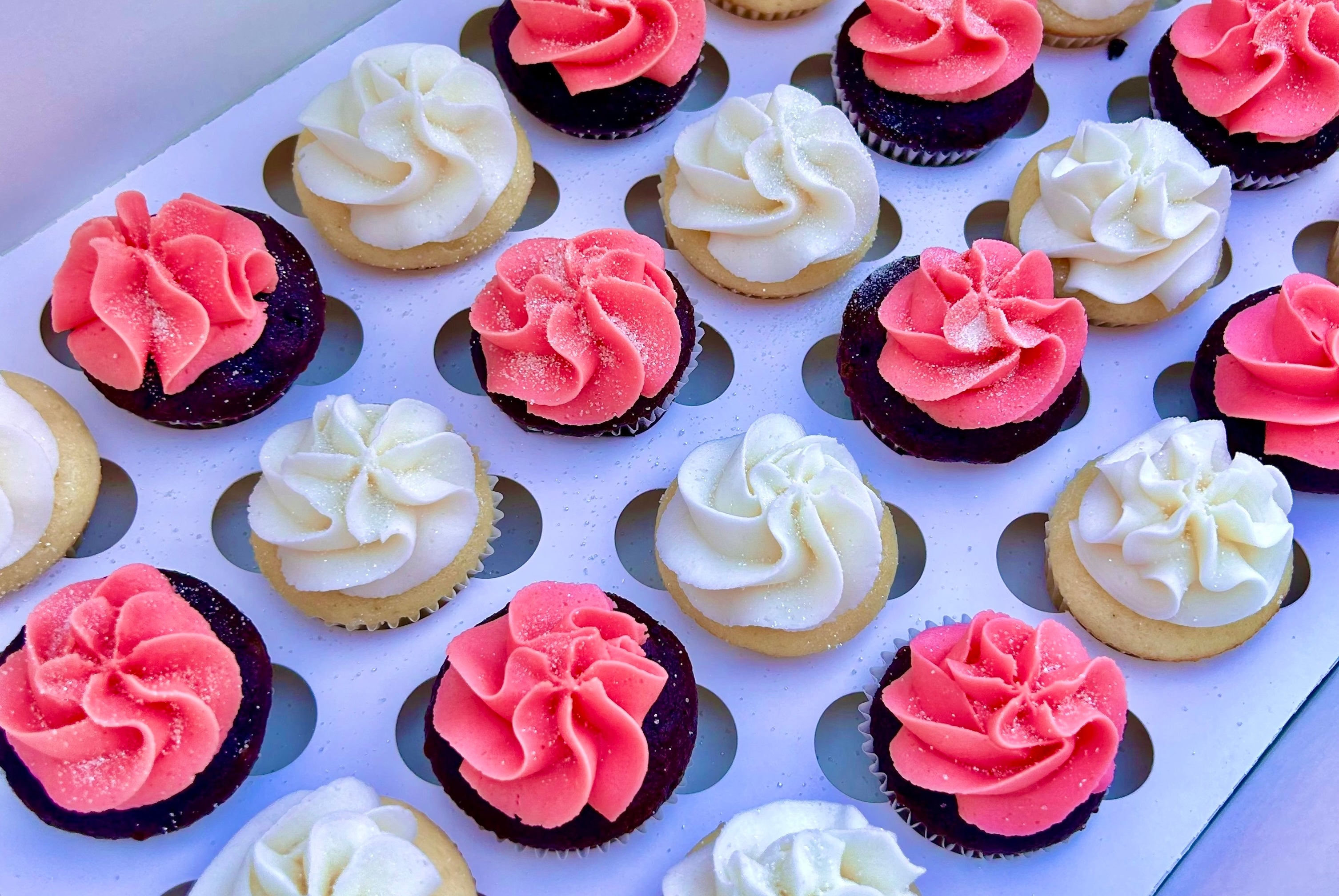 Assorted cupcakes with pink and white frosting in a white box.