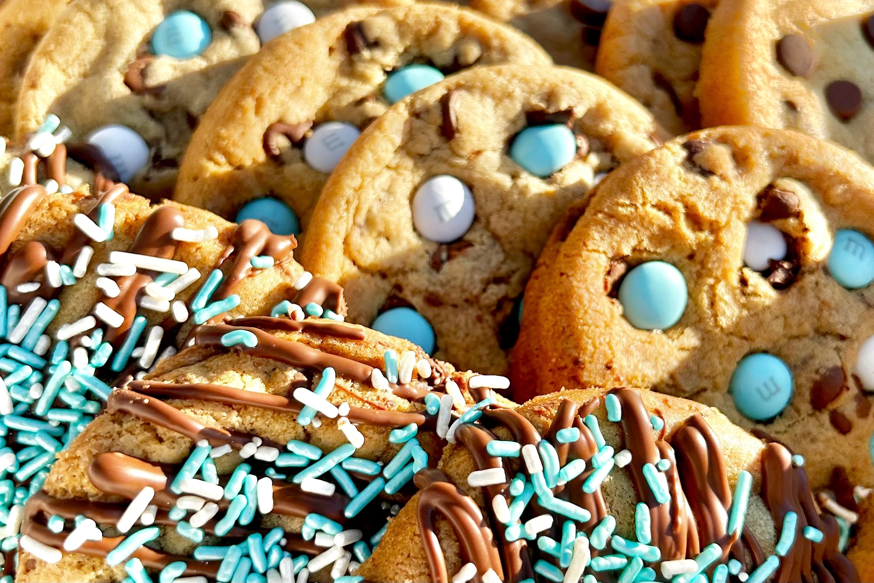 Close-up of light blue M&M cookies and light blue sprinkle cookies with chocolate drizzle.