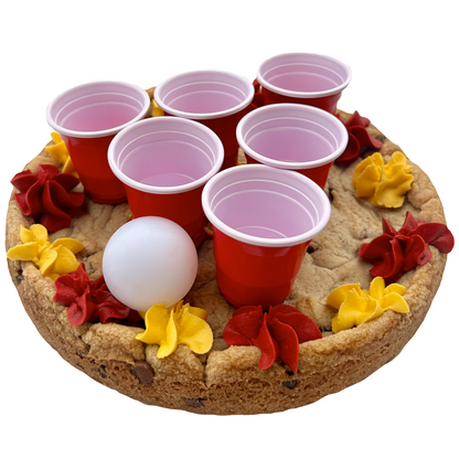 Maroon and gold cookie pong cake with mini red cups, ping pong ball, and maroon and gold frosting.