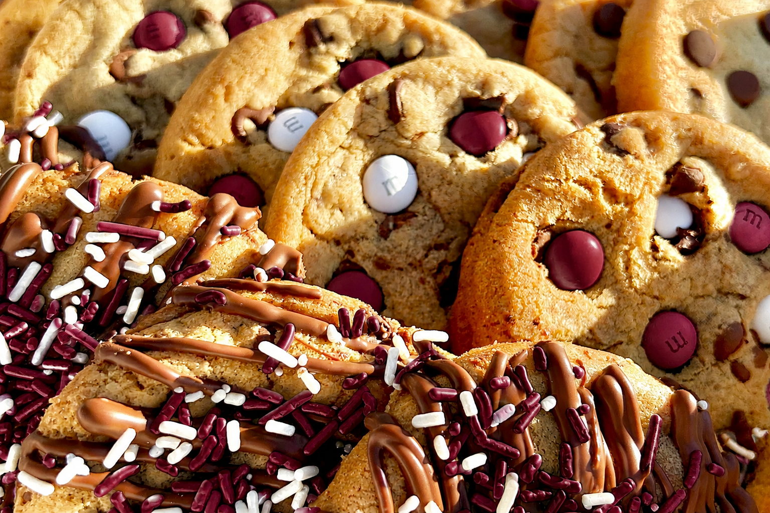 Close-up of maroon M&M cookies and maroon sprinkle cookies with chocolate drizzle.