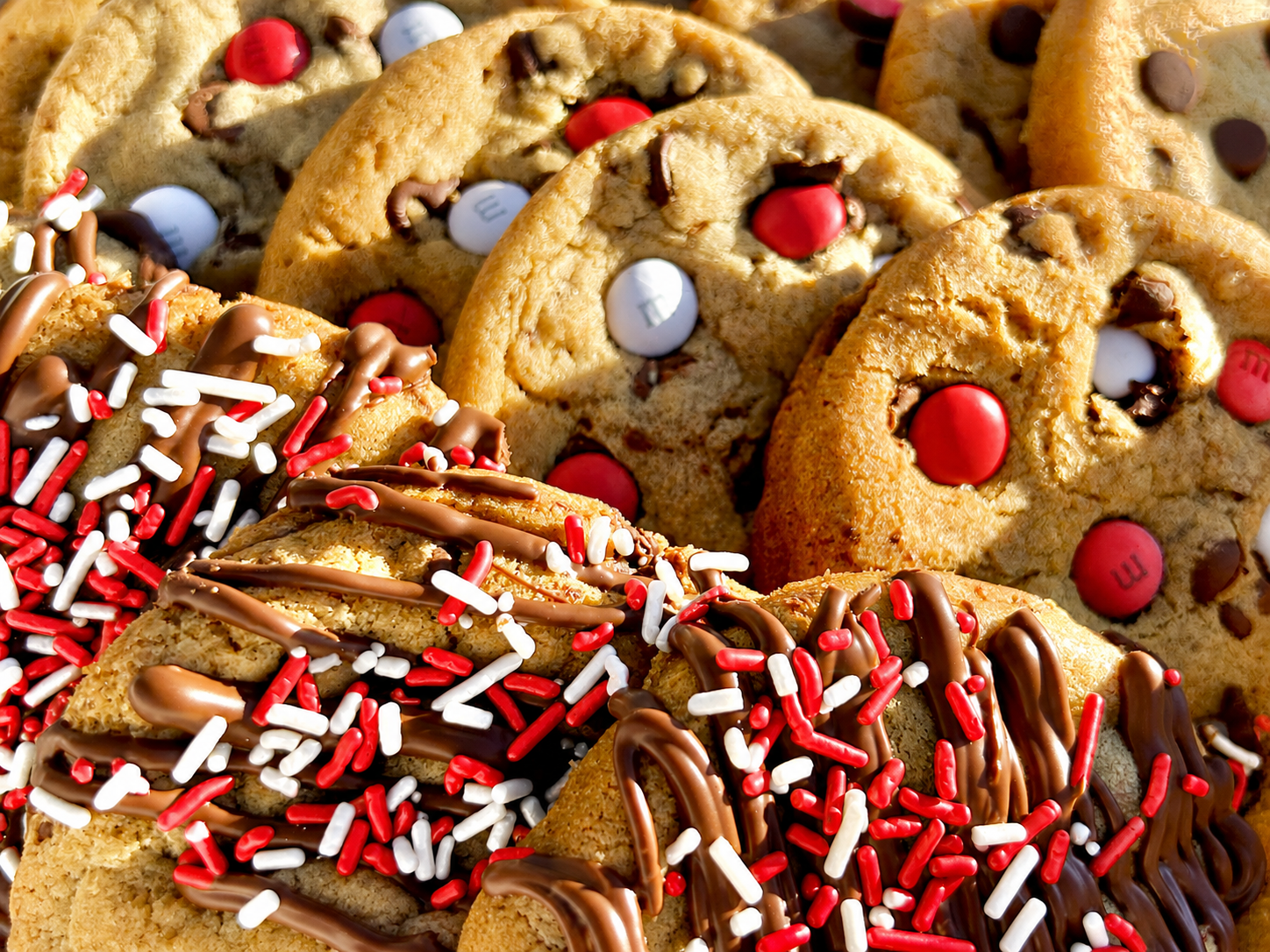 Close-up of red M&M cookies and red sprinkle cookies with chocolate drizzle.