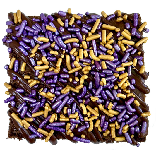 Purple and gold sprinkle brownie with chocolate drizzle and purple and gold sprinkles.