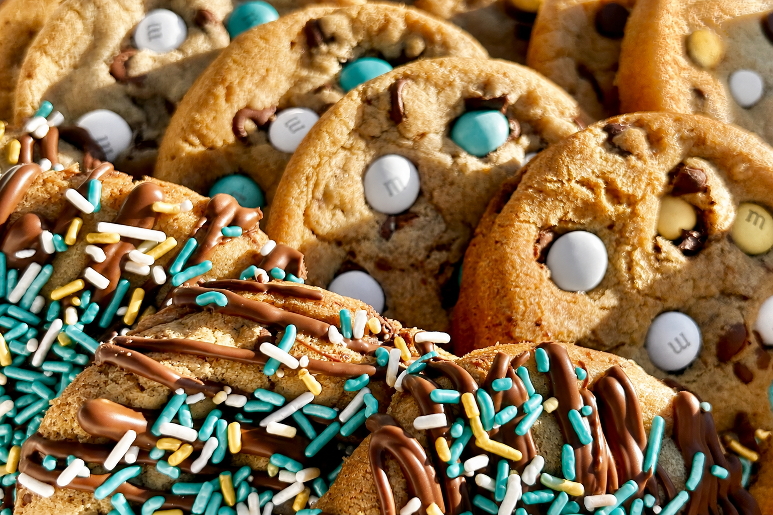 Close-up of teal M&M cookies and teal sprinkle cookies with chocolate drizzle.