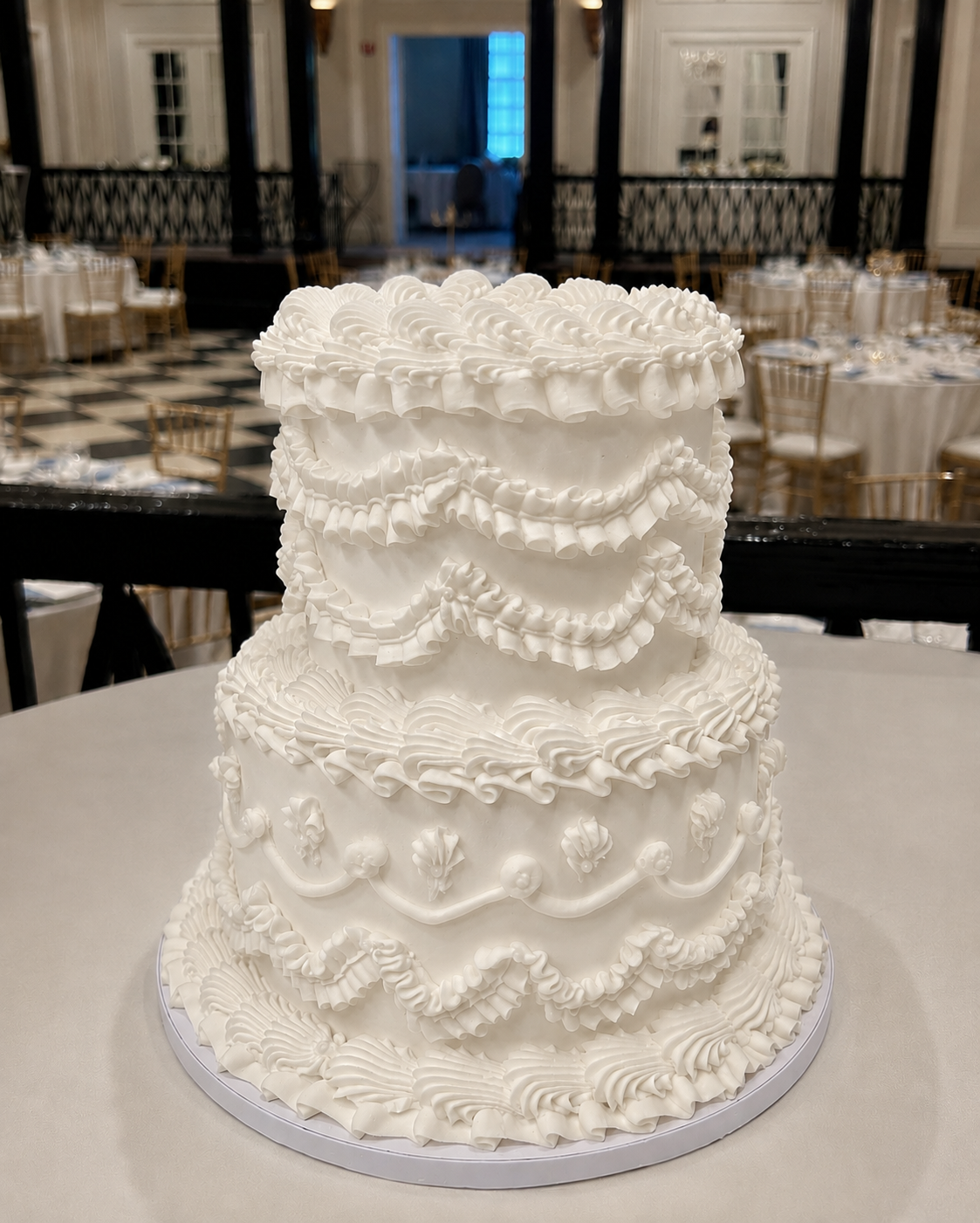 Two-tiered white wedding cake with intricate designs in a banquet hall setting.