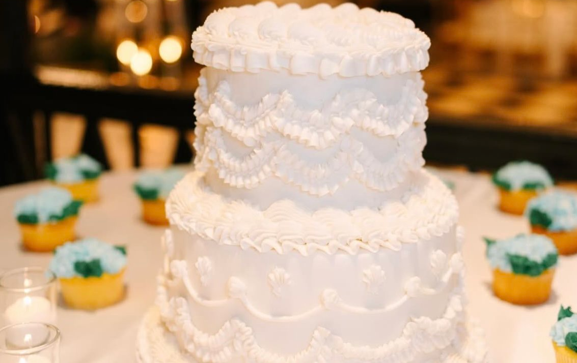 White wedding cake with on a table with light blue hydrangea cupcakes around it.