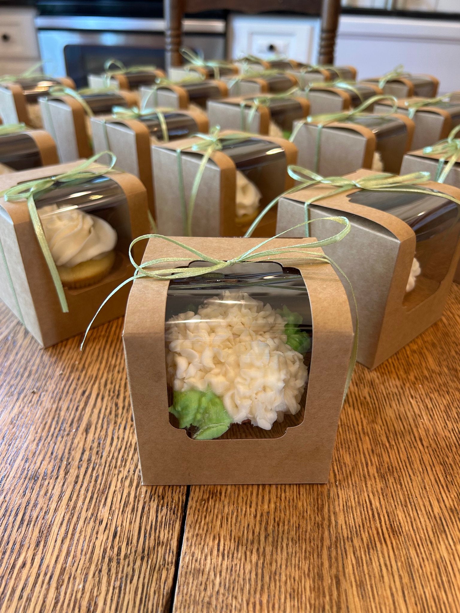 Small brown gift boxes with clear window lids containing a white cupcake.