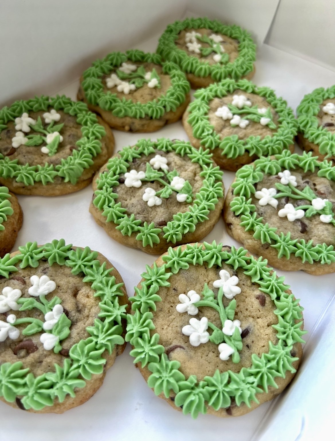 Cookies with green icing and white flowers in a white bakery box.