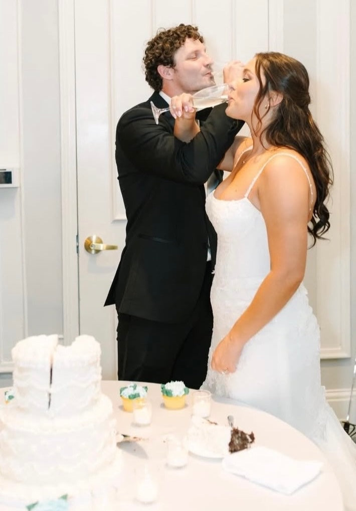 Bridge and groom drinking champagne behind white wedding cake with two light blue hydrangea cupcakes.