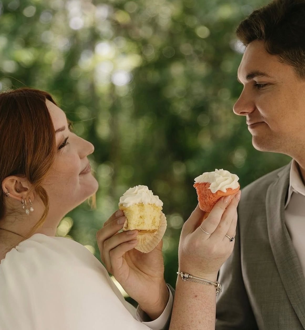 Bride and groom holding cupcakes and smiling at each other.